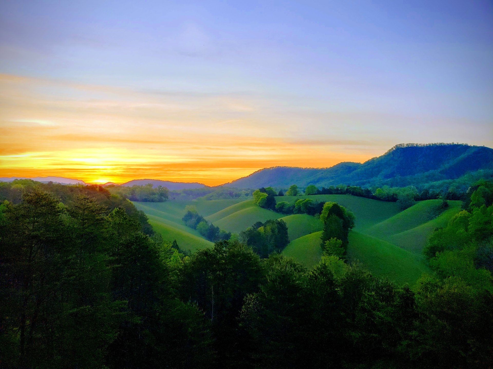 A sunset over a lush green valley with mountains in the background.