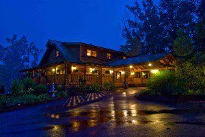 A large log cabin is lit up at night in the rain.