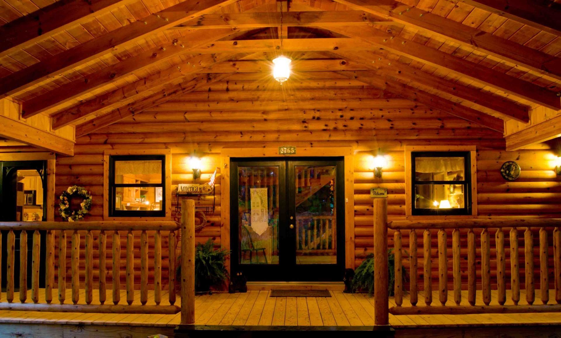 The front of a log cabin with a porch and a ceiling fan.