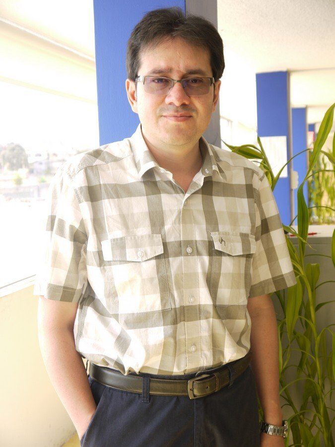 Un hombre con gafas y camisa a cuadros está de pie con las manos en los bolsillos.
