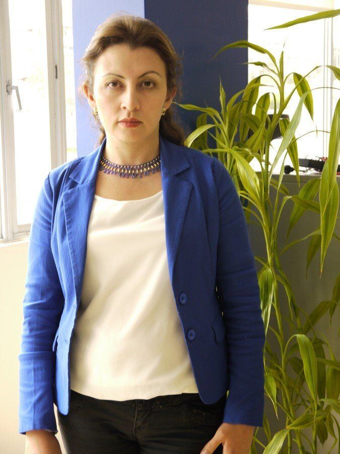 Una mujer con una chaqueta azul está parada frente a una planta.