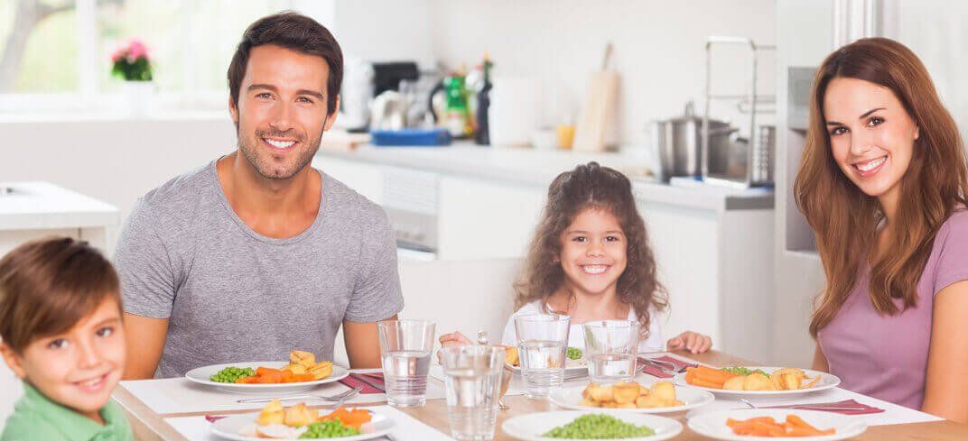 Una familia está sentada en una mesa con platos de comida.