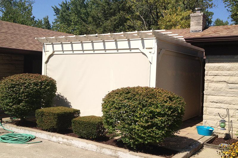 A white shed is surrounded by bushes and a hose