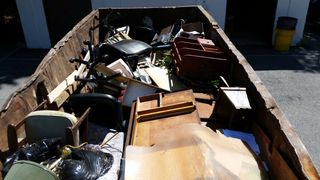 A dumpster filled with furniture and trash bags