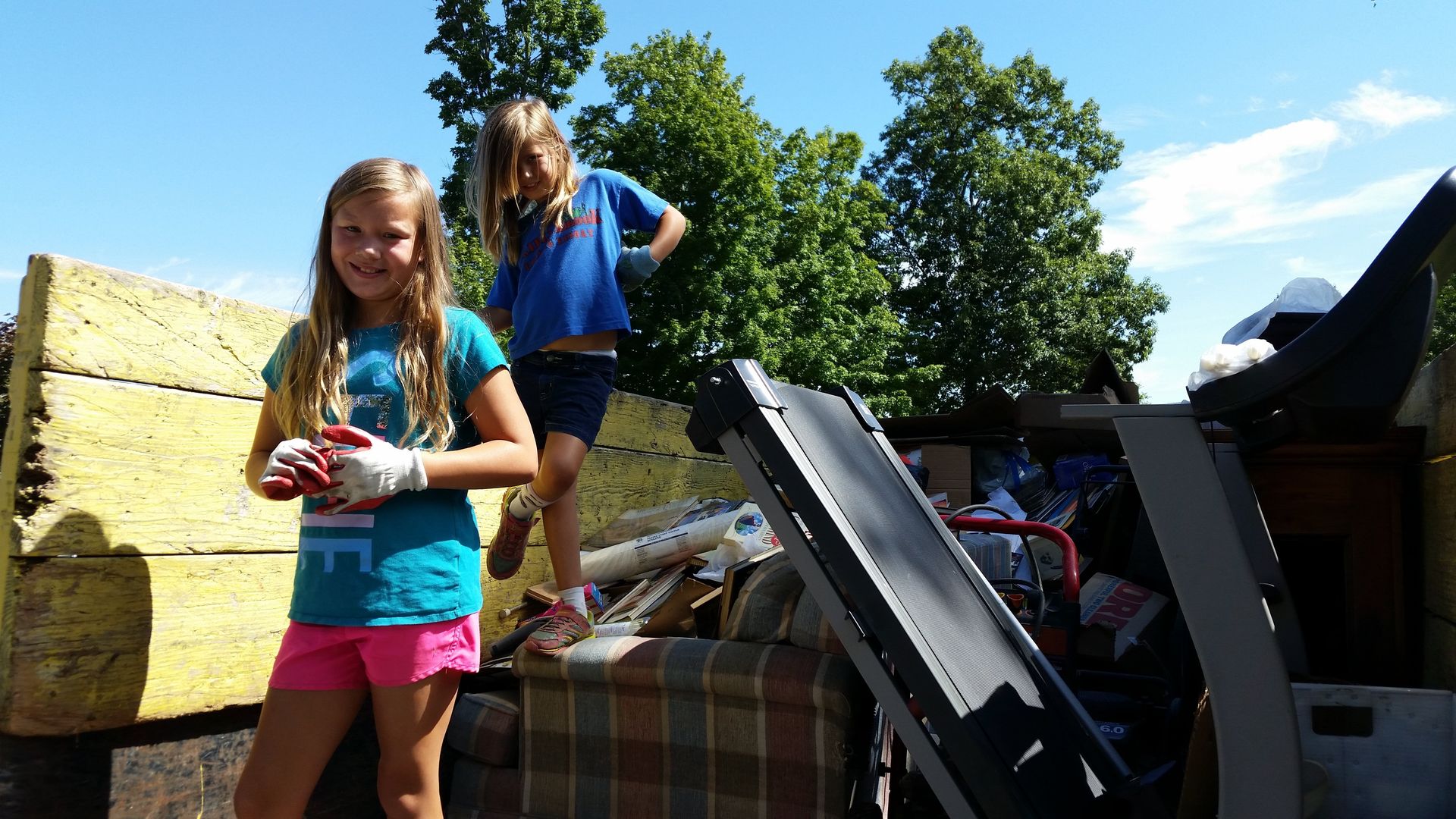 Two young girls are standing in front of a pile of junk.