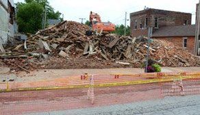 A pile of rubble is sitting on the side of the road in front of a building being demolished.
