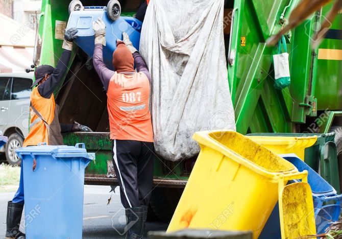 Two garbage collectors are loading garbage into a garbage truck.