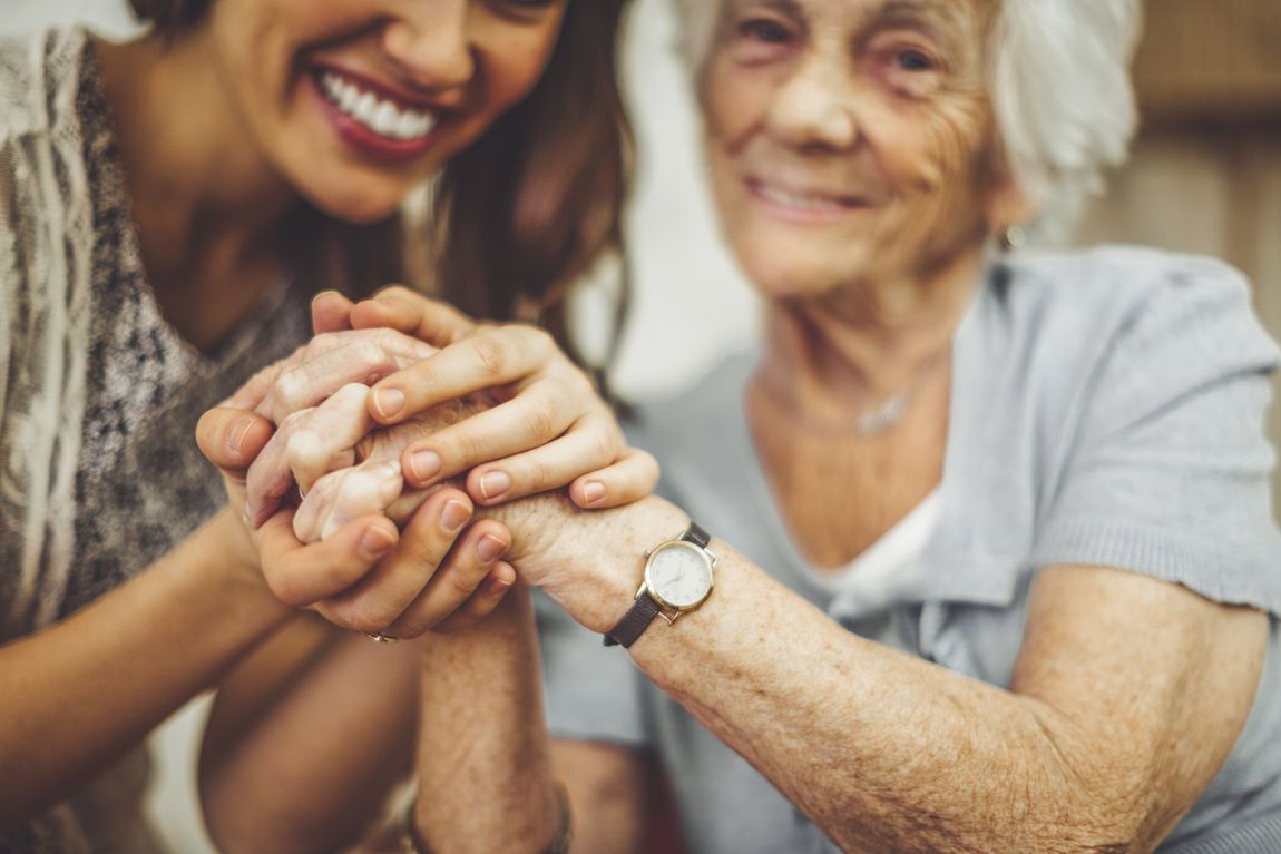 Woman holding hands with older person, both smiling.