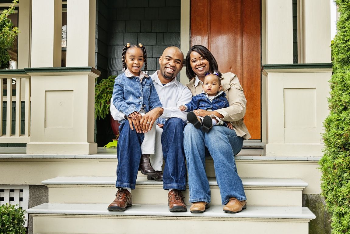 Family of four smiles on porch steps of a house.