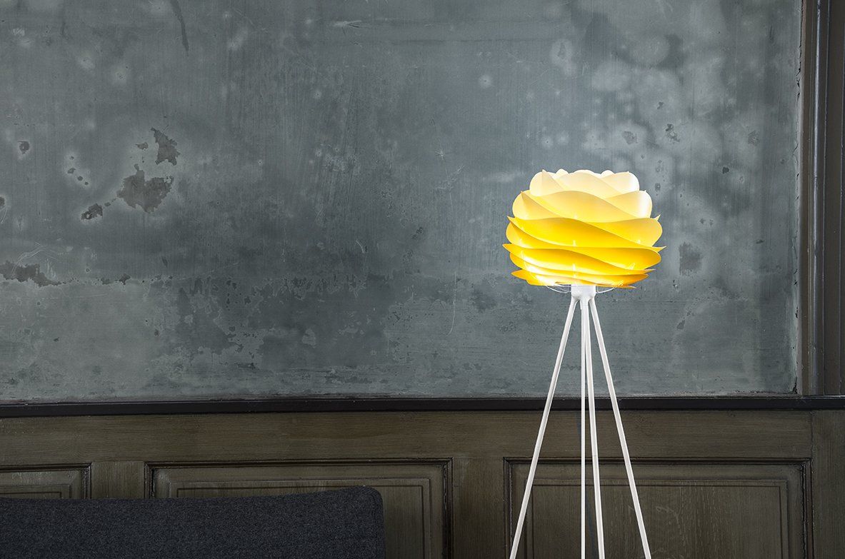 A yellow lamp is sitting on a tripod in front of a wall.