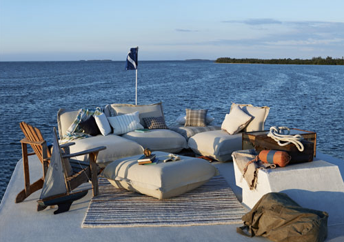 A dock with a couch , chairs , ottoman , and a boat model in the water.