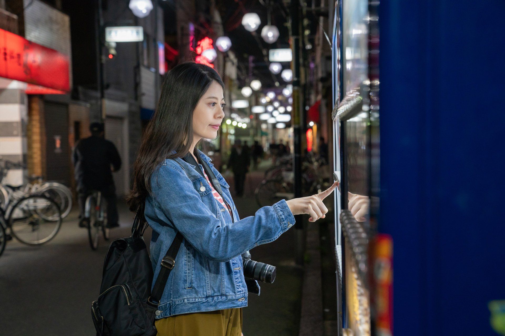Young woman using a self-service machine on a busy city street at night.