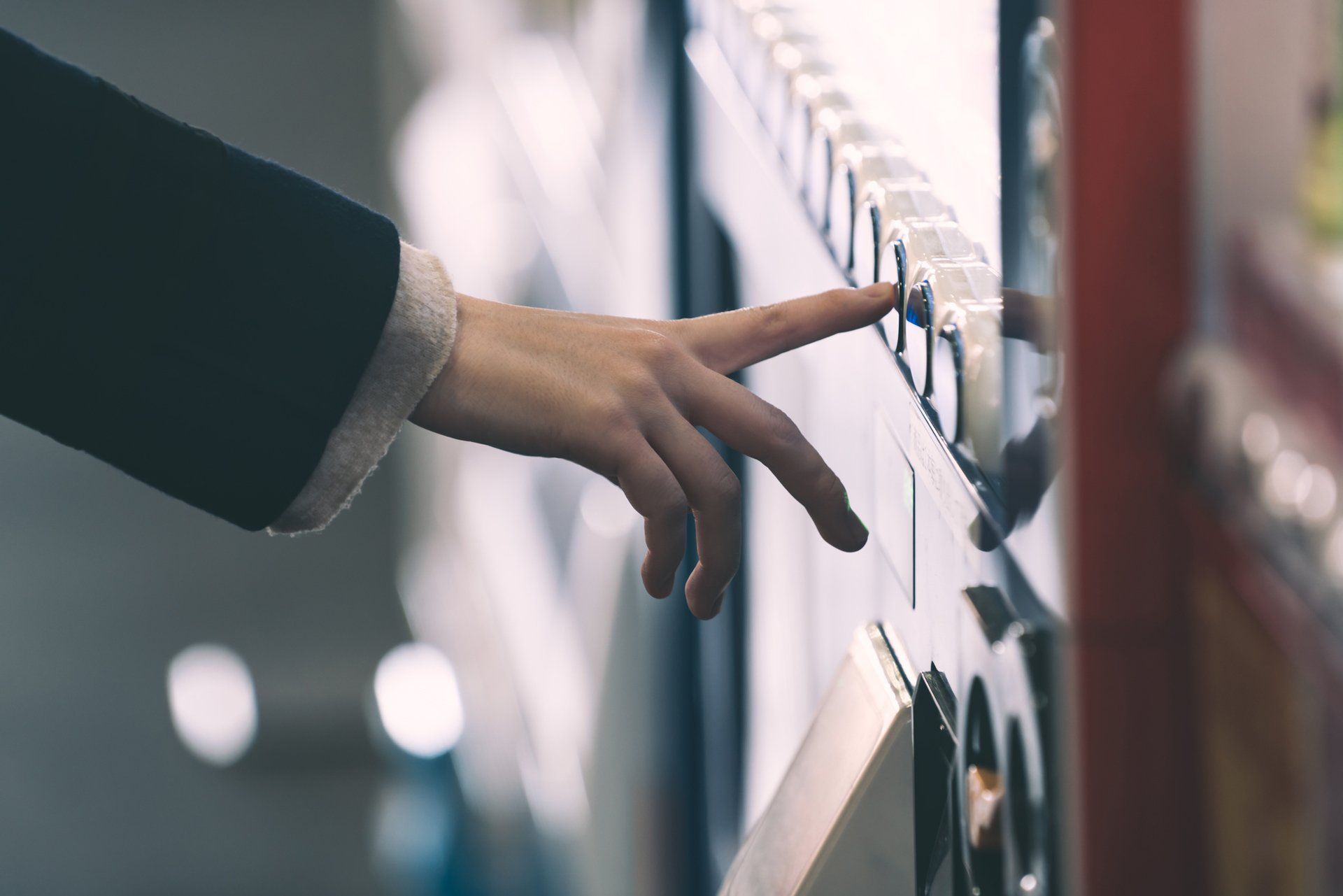 A person's hand reaching to press a button on a vending machine.