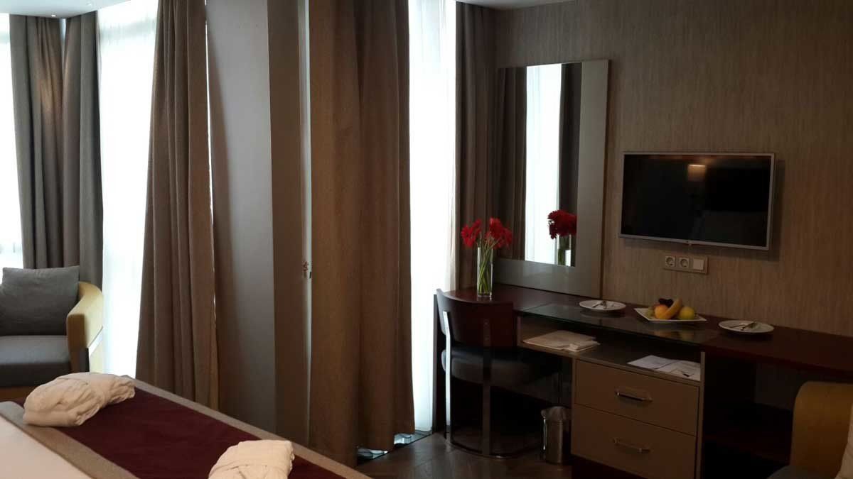 Yatak, çalışma masası, sandalye ve televizyonun bulunduğu bir otel odası.