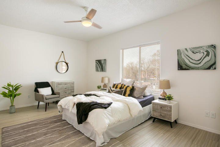 A bedroom with a bed , nightstand , chair and ceiling fan.