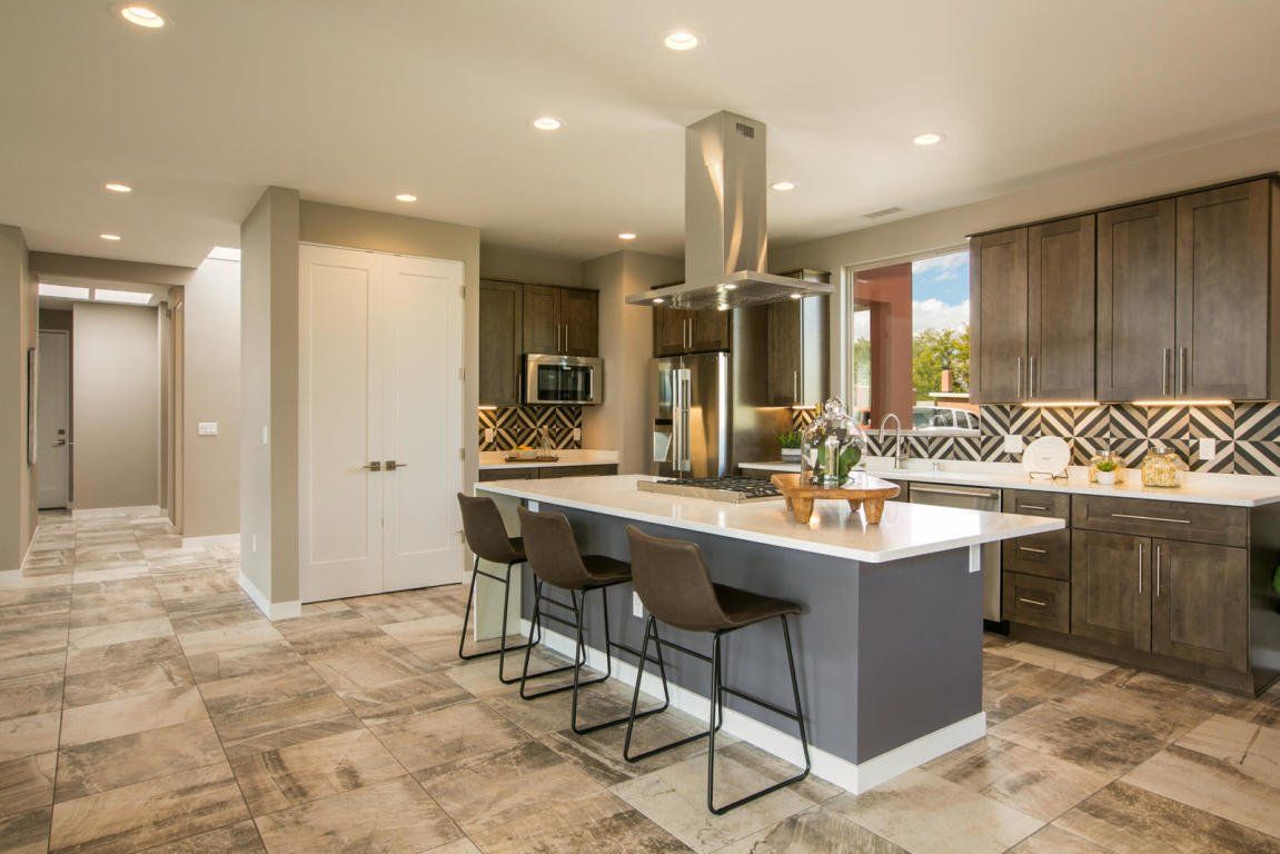A kitchen with a large island , stools and a refrigerator.