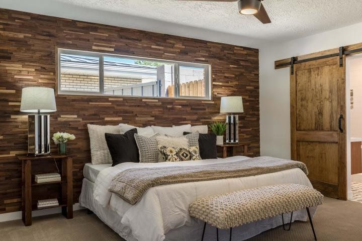 A bedroom with a bed , lamps , a ceiling fan and a sliding barn door.