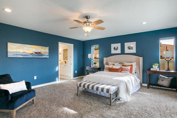 A bedroom with blue walls , a bed , a chair and a ceiling fan.