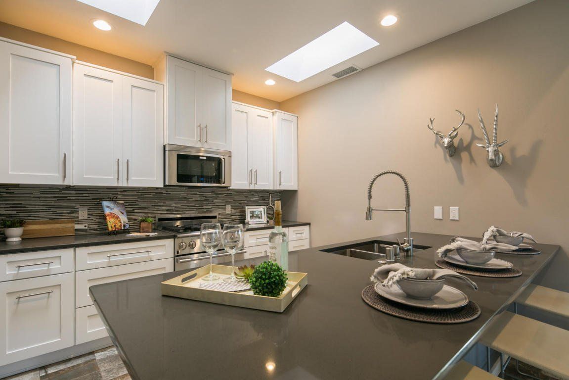 A kitchen with white cabinets , stainless steel appliances , a sink , and a large island.