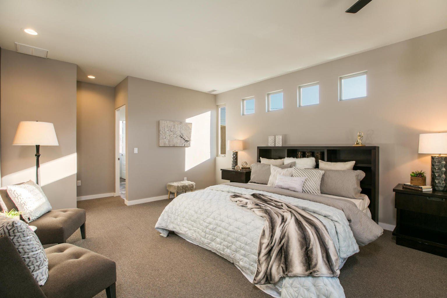 A bedroom with a large bed , chairs , lamps and a ceiling fan.