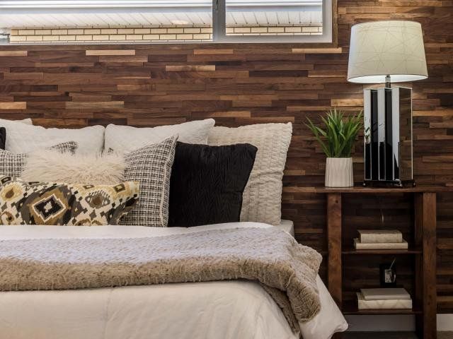 A bedroom with a bed , nightstand , lamp and wooden wall.