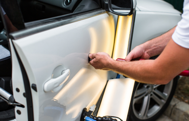 Person applying paint protection film to a white car door with a squeegee
