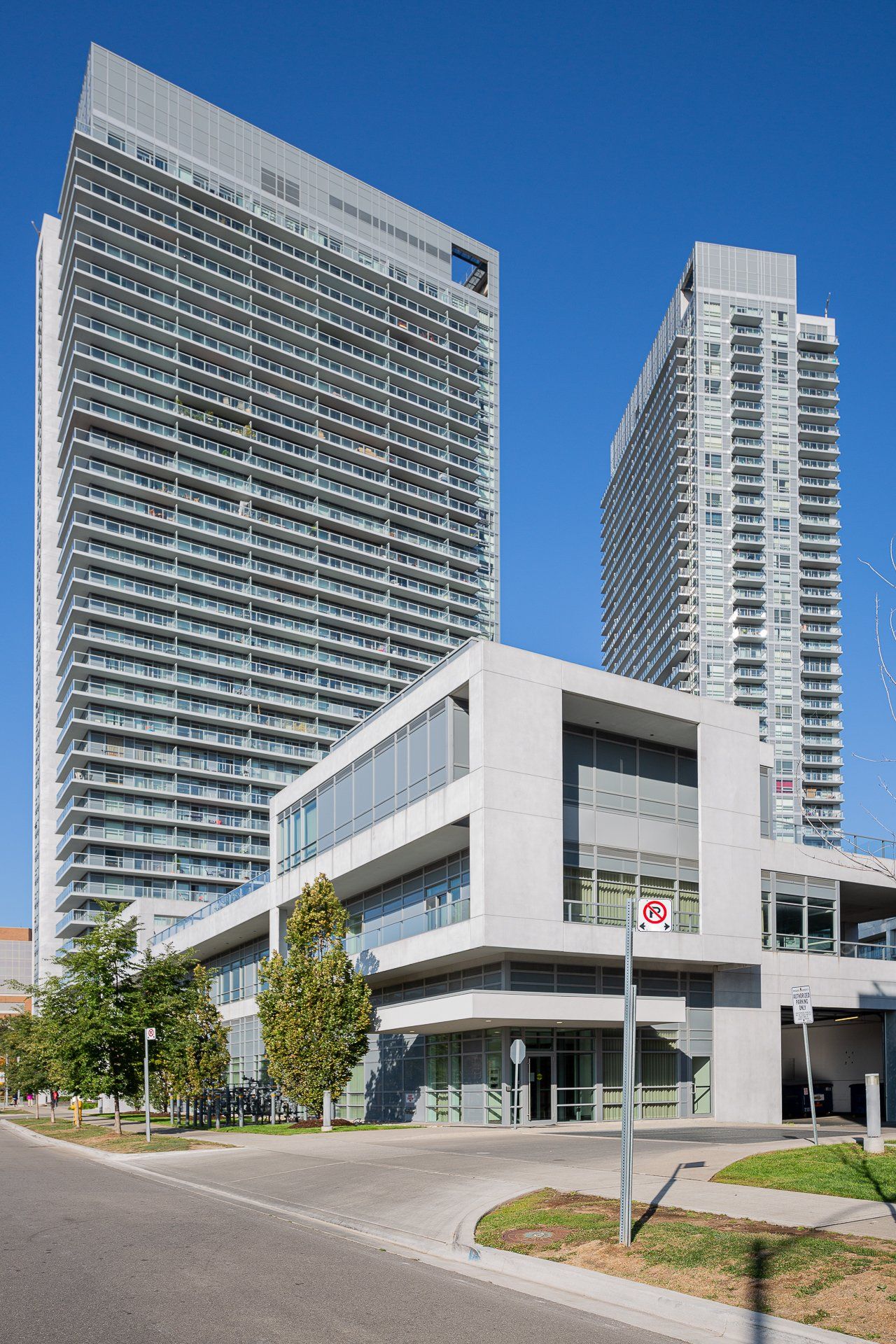 A low-rise modern concrete building with large windows stands in front of two tall, glass-clad residential towers.