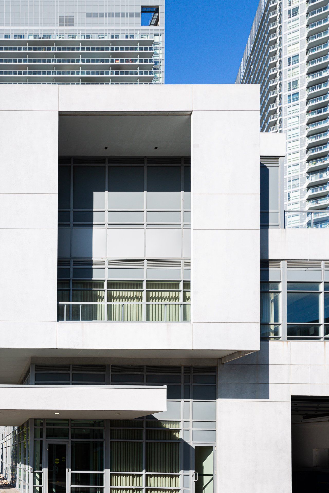A modern building with a white geometric facade, large glass windows, and a tall skyscraper visible in the background.