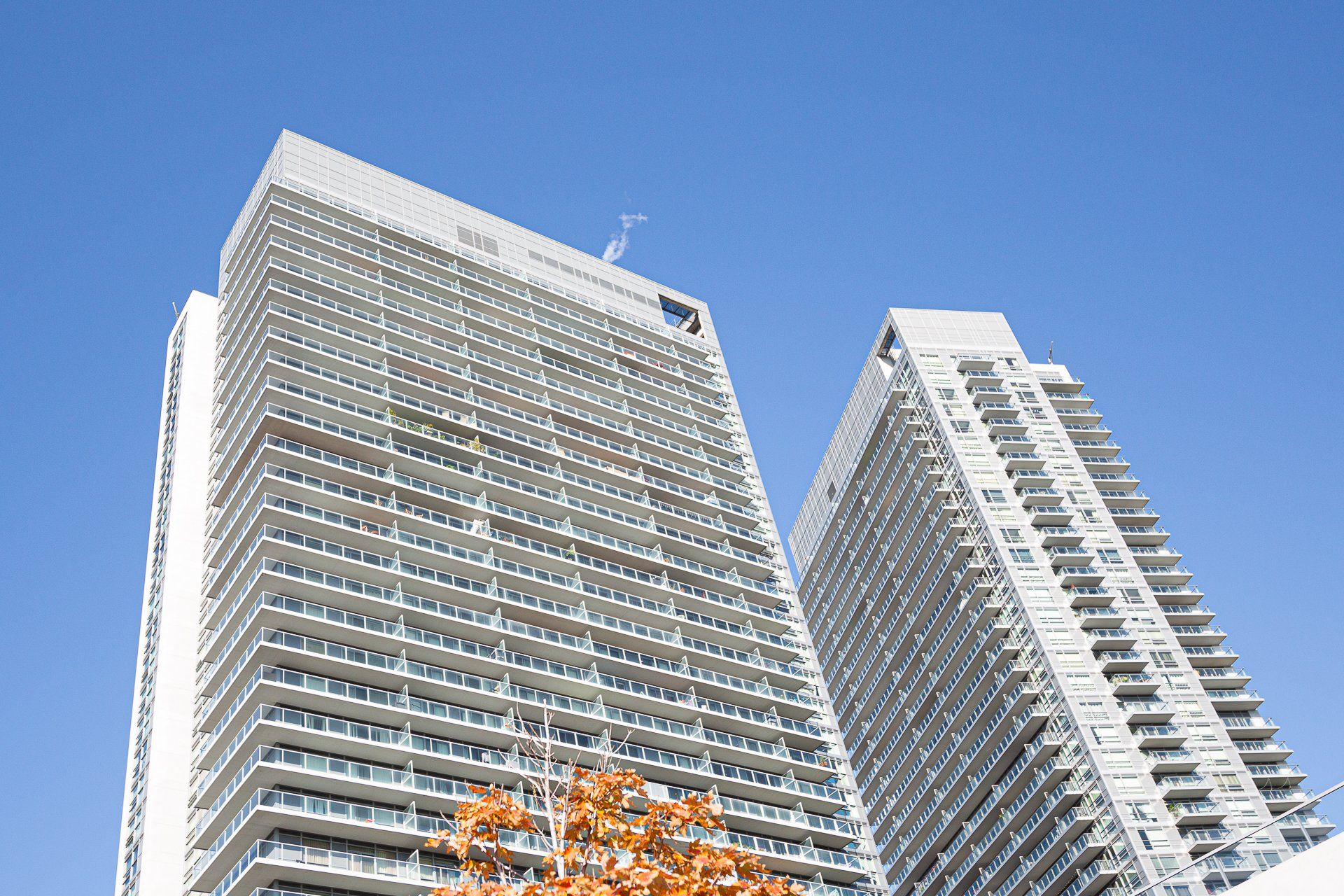 Two tall, modern high-rise apartment buildings with balconies against a clear blue sky.