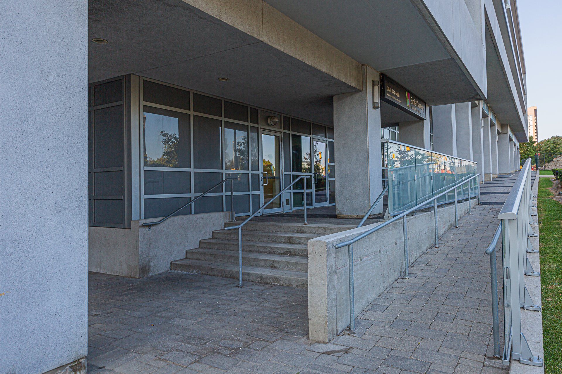 A building entrance featuring a set of concrete steps with a metal railing alongside an accessible concrete ramp.
