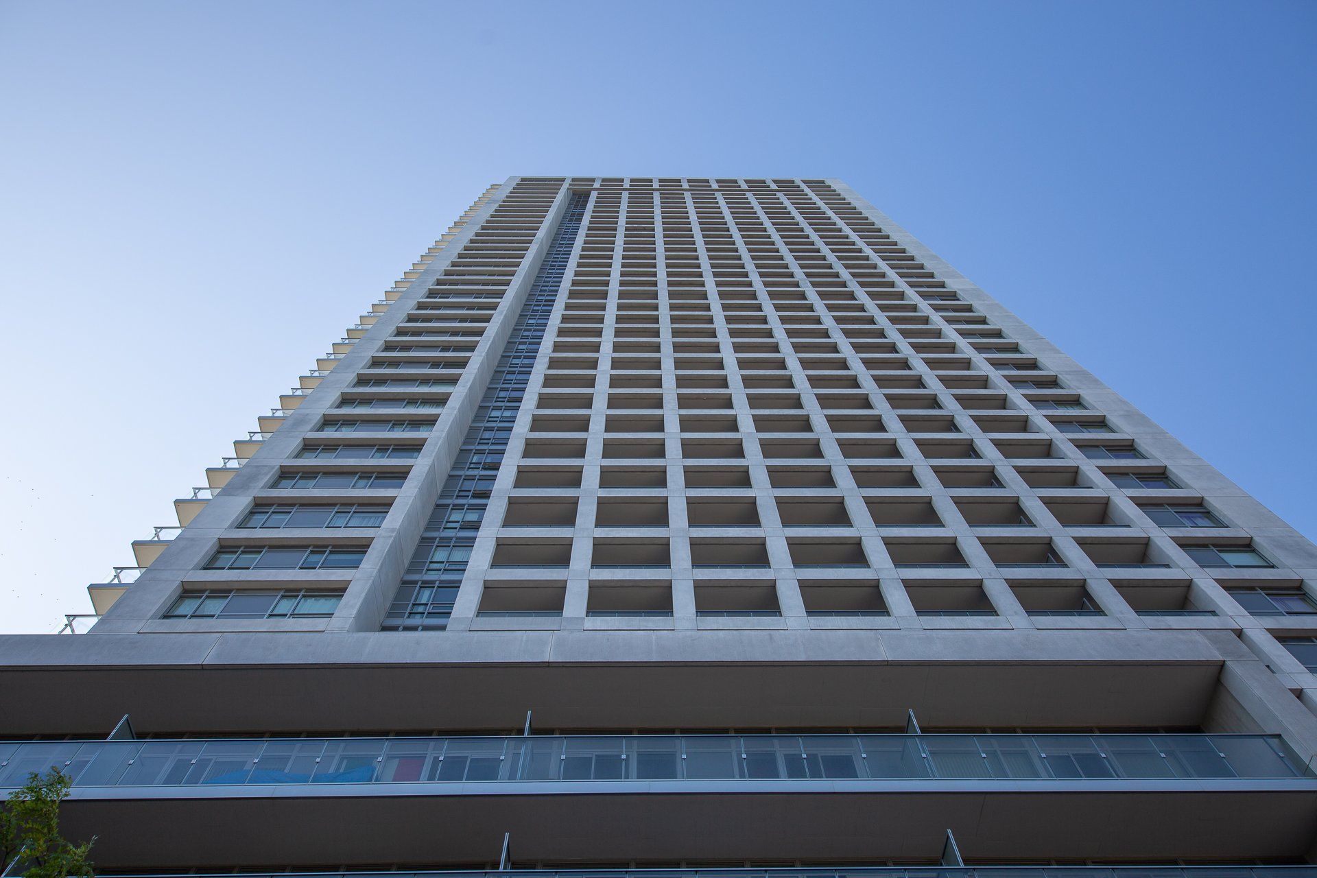 A low-angle view of a tall, modern, concrete apartment building with many identical rectangular balcony windows.