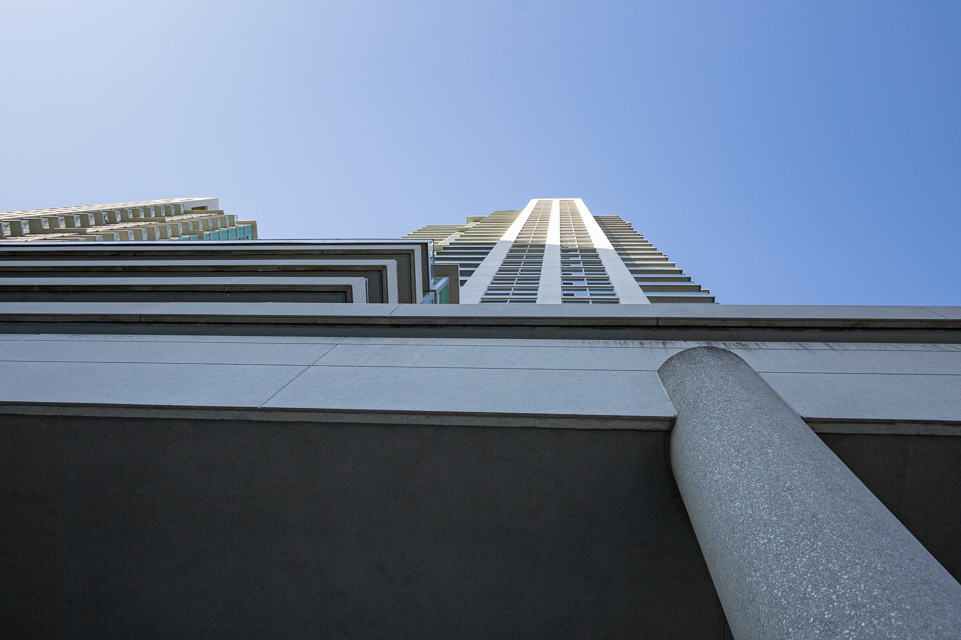 Low-angle shot of a modern apartment building exterior rising into a bright, clear blue sky.