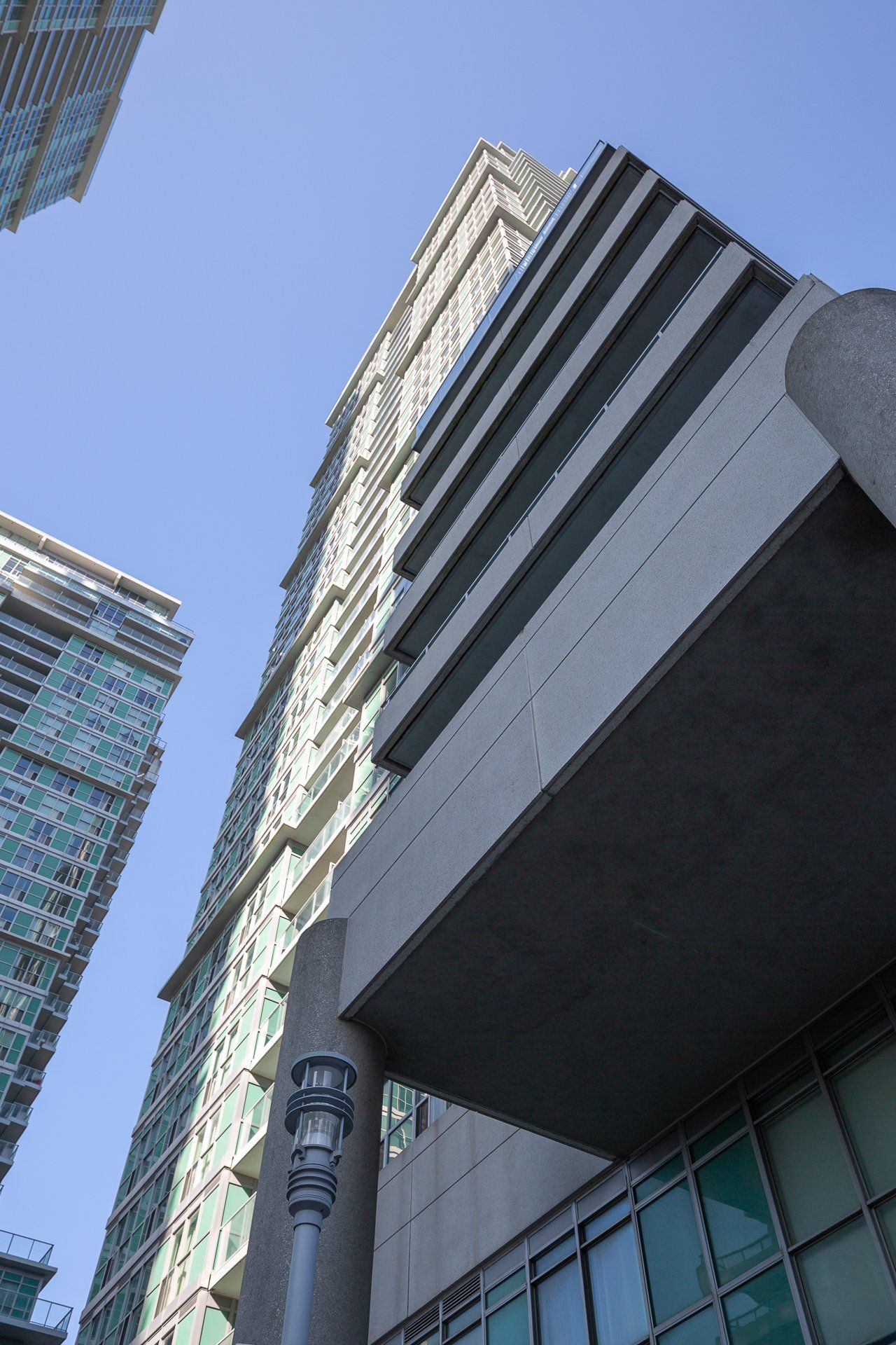 Low-angle view of a modern high-rise building with a glass facade, balconies, and a prominent concrete entrance overhang.