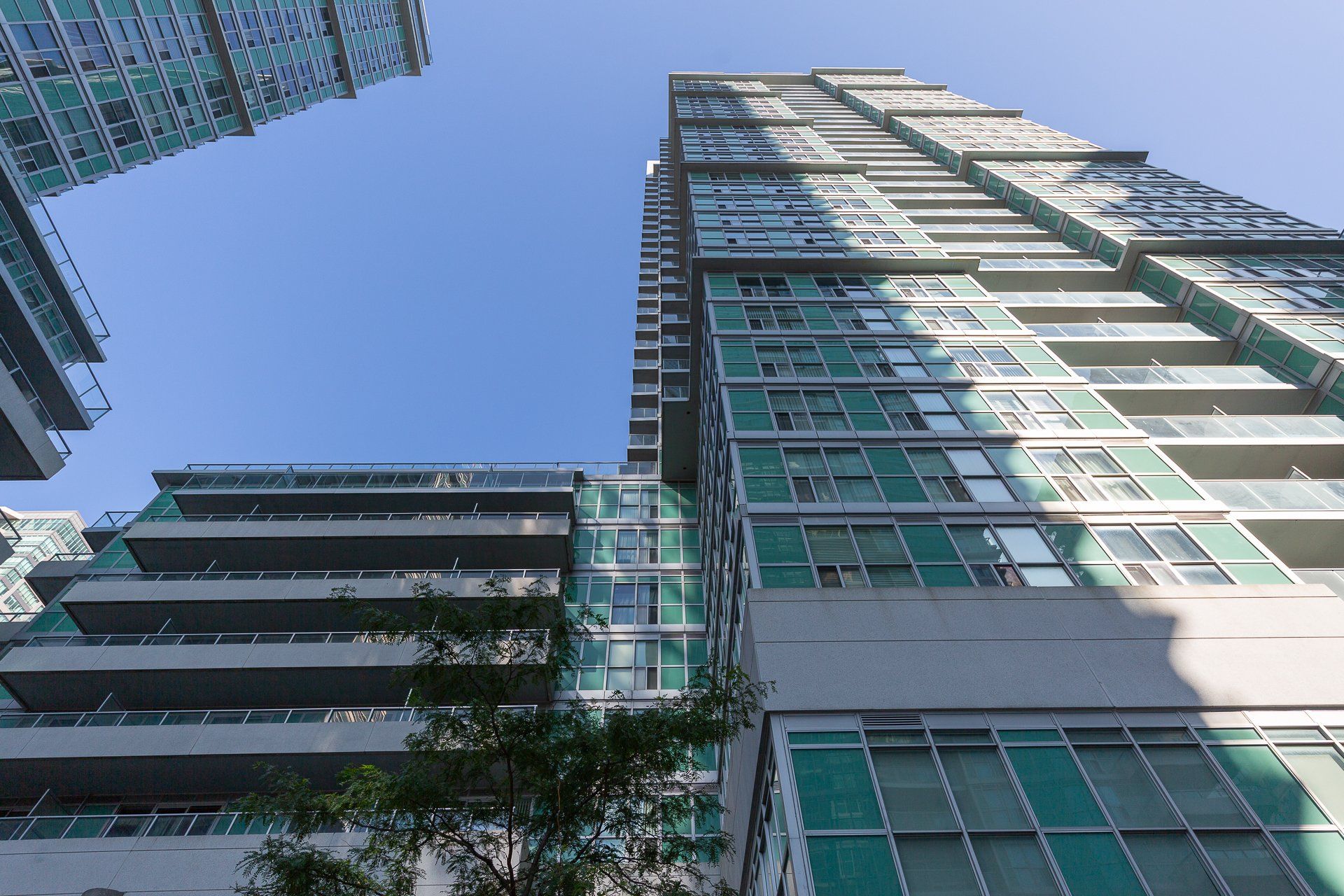 Low-angle view of two modern residential high-rise buildings with glass and concrete facades against a clear blue sky.