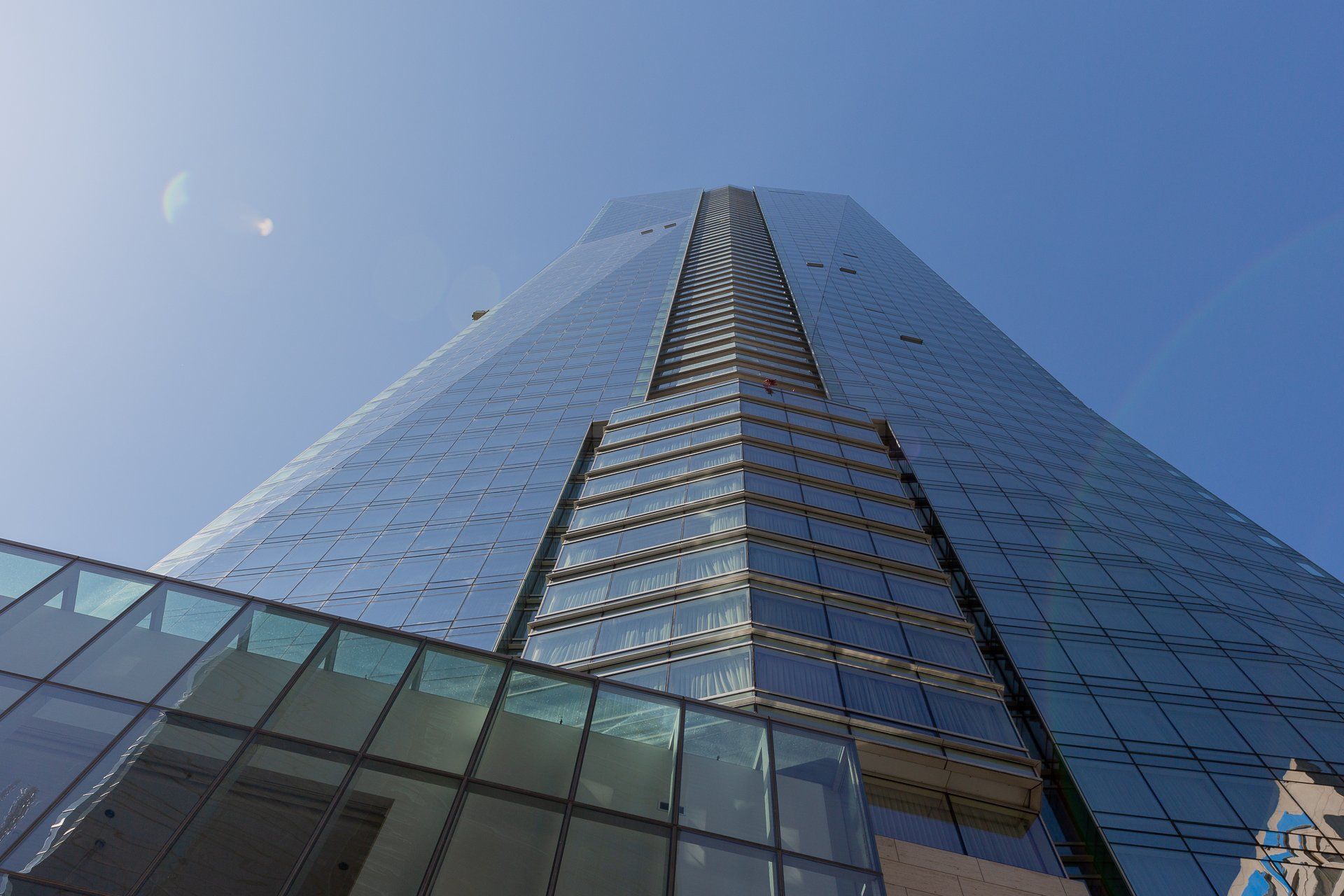 A low-angle view of a modern glass skyscraper with a central decorative facade against a clear blue sky.