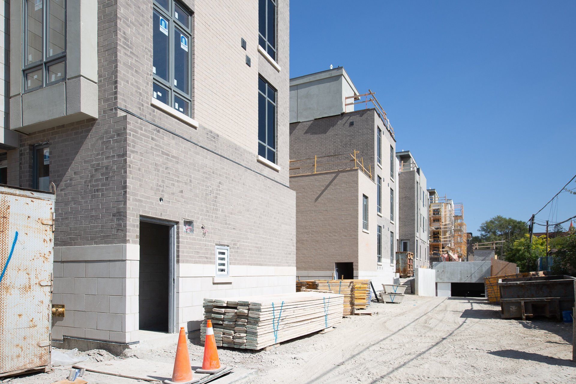 Construction site with several beige brick townhouse structures, a gravel ground, and orange traffic cones in the front.