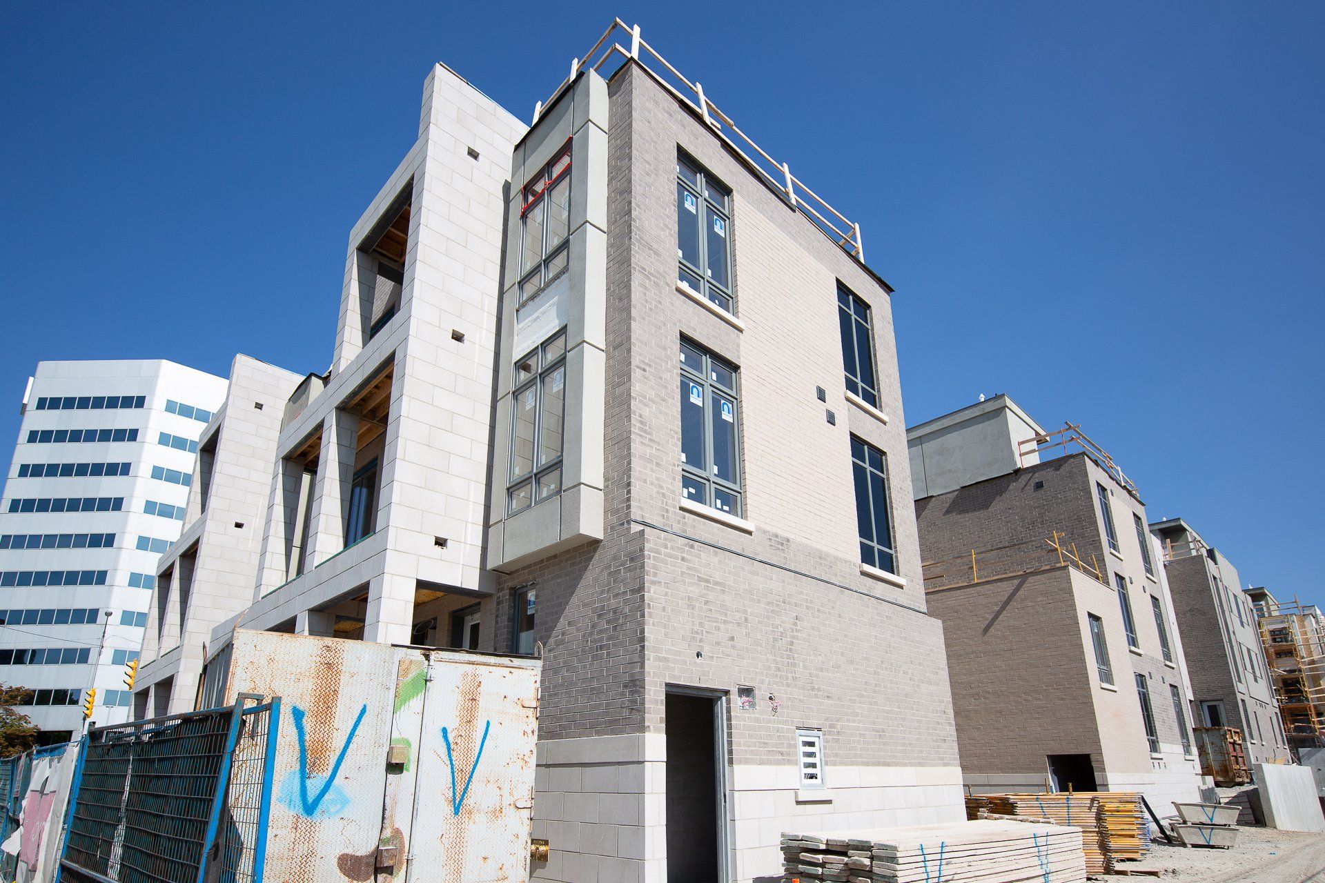A row of modern, light-colored brick townhomes under construction under a clear blue sky.