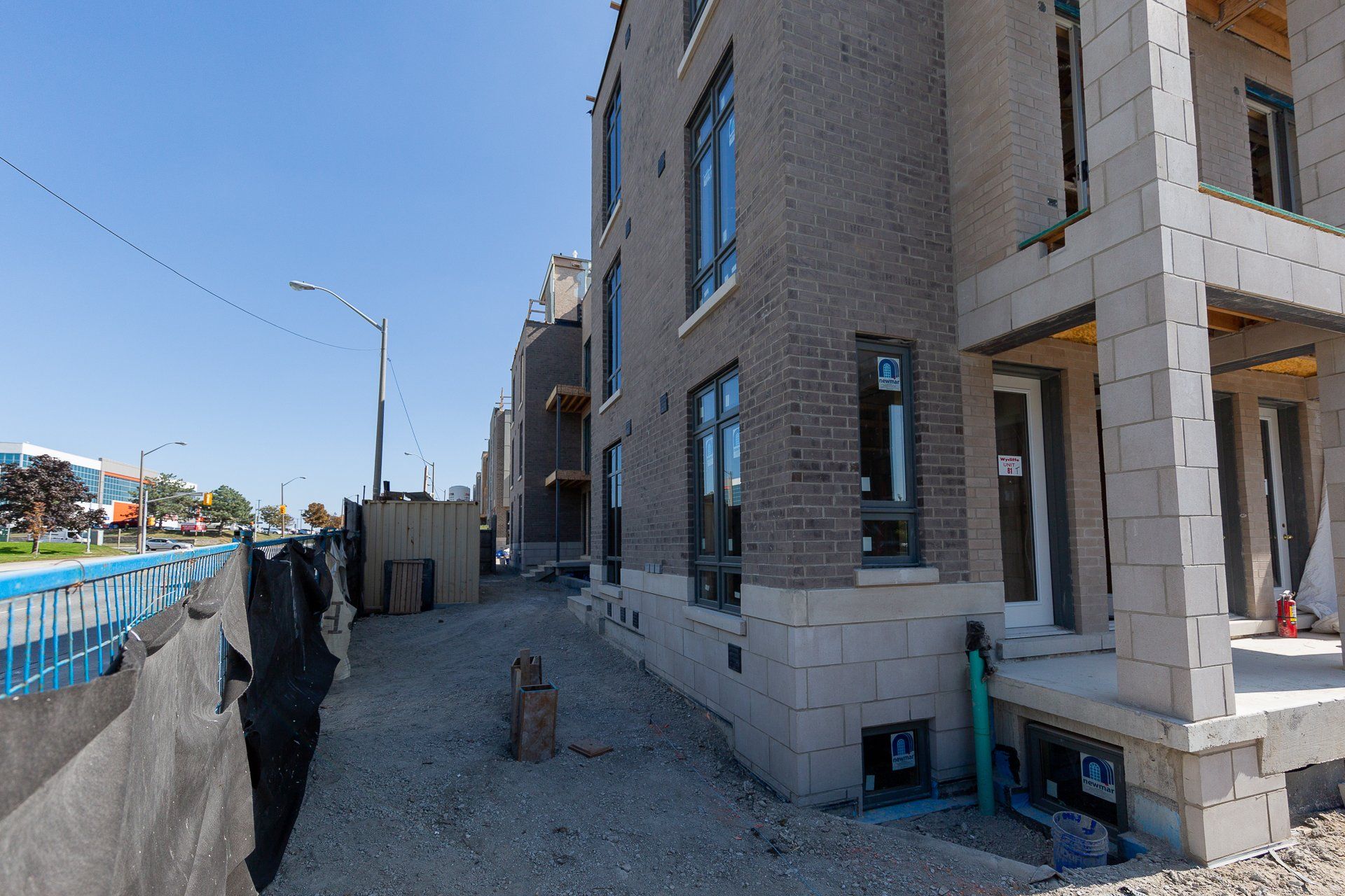 A multi-story brick townhouse under construction, with exposed concrete blocks and gravel on a sunny day.