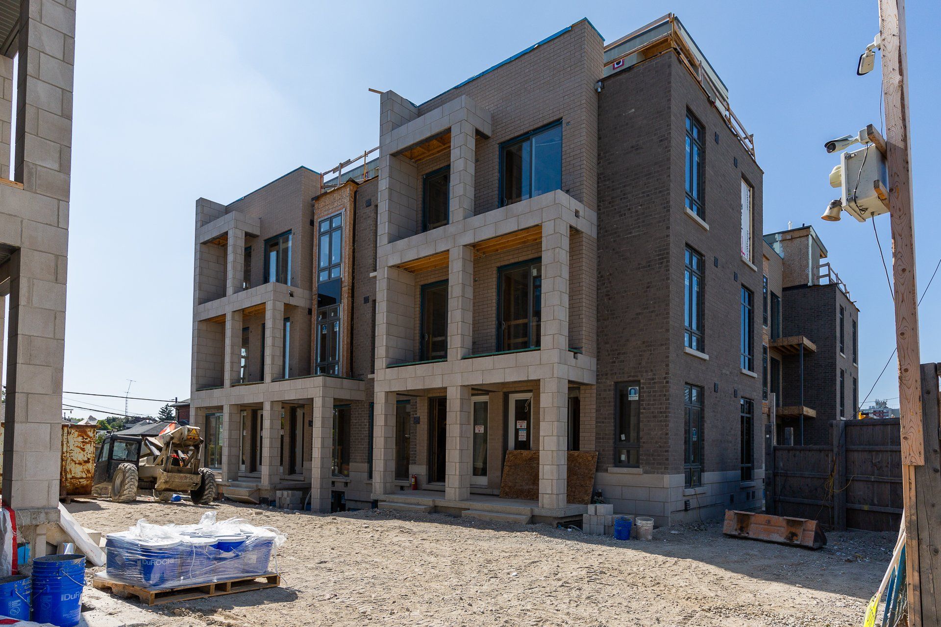 A modern multi-story brick apartment building under construction on a sunny day with building supplies in the foreground.