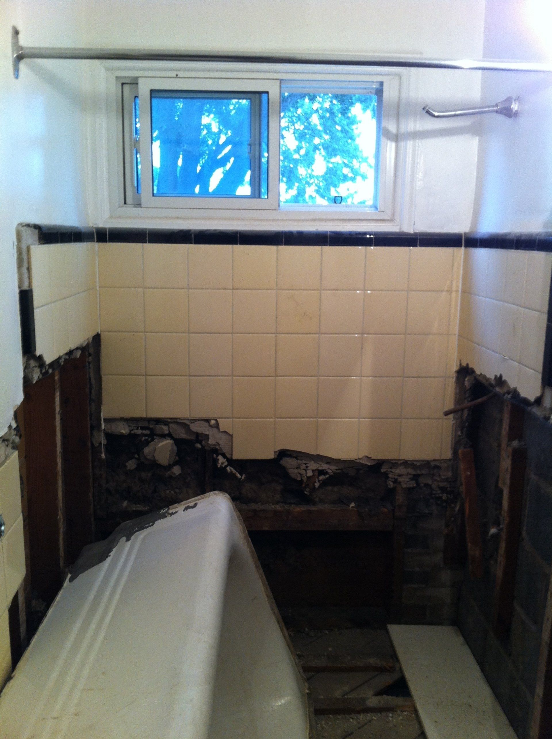 A bathroom under renovation with exposed wall studs and missing tiles around a bathtub.