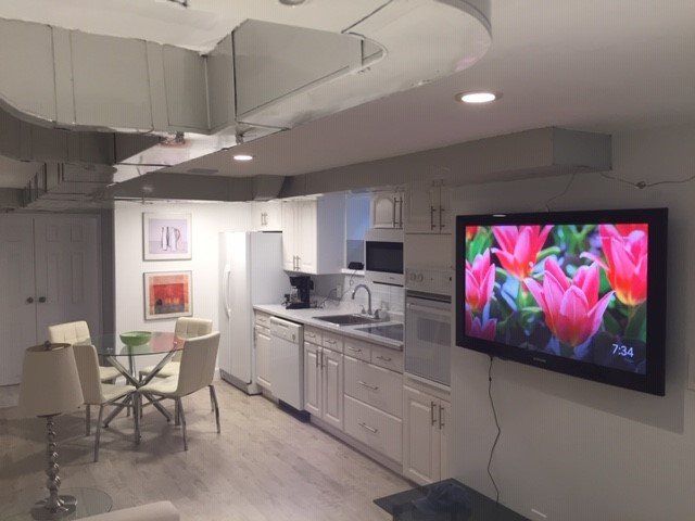 A brightly lit, modern kitchen and dining area with white cabinets, a small glass table, and a wall-mounted television.