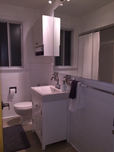 A small bathroom with a white vanity, a toilet, a window, and a large mirror reflecting a shower curtain.