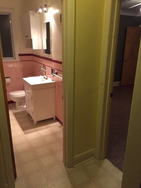 A view from a doorway into a small bathroom with pink tiled walls, a white vanity, and a toilet.