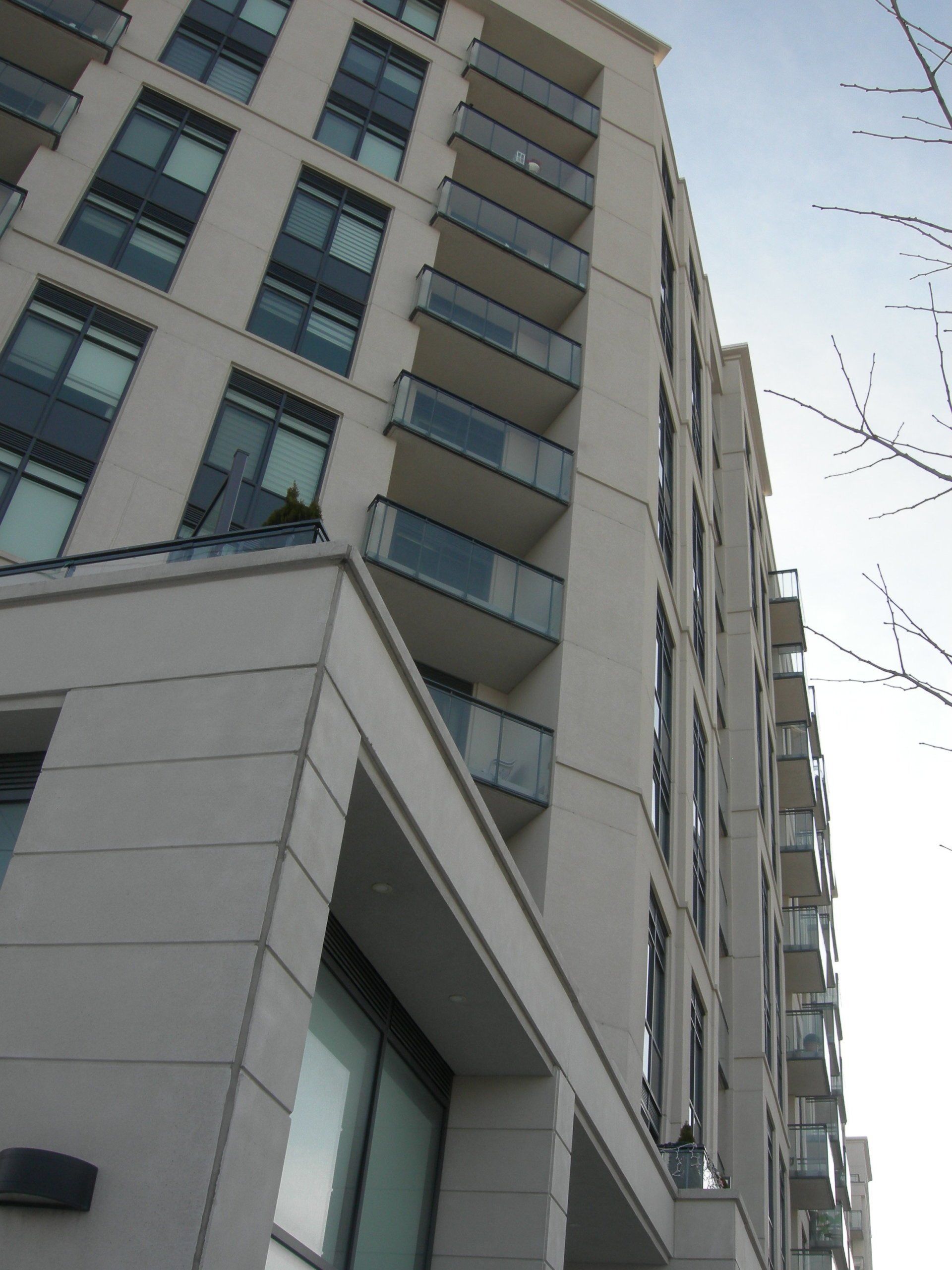 Low-angle view of a modern, multi-story beige apartment building with glass balconies, reaching toward the sky.
