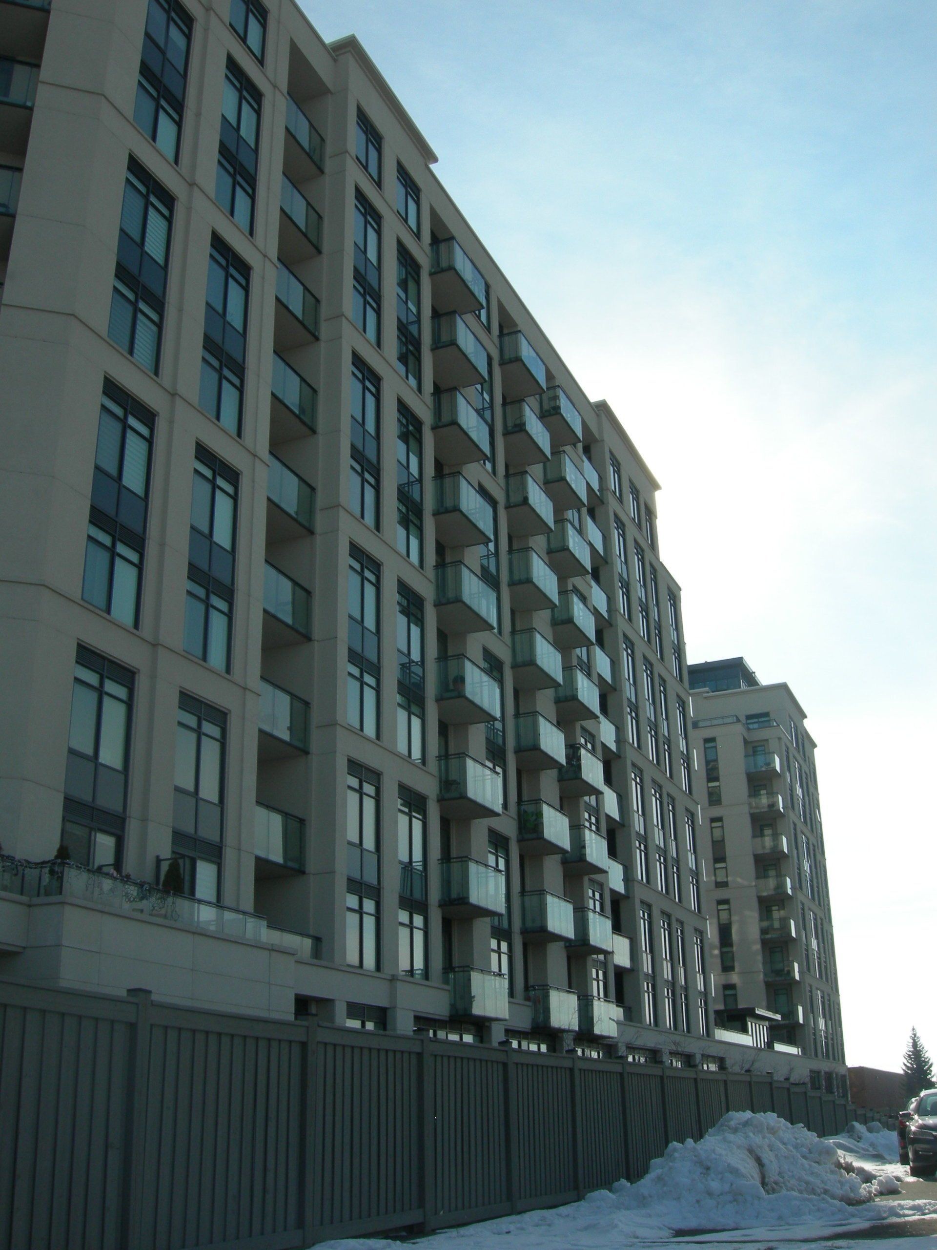 A tall, light-colored apartment building with balconies and large windows viewed from below against a bright sky.