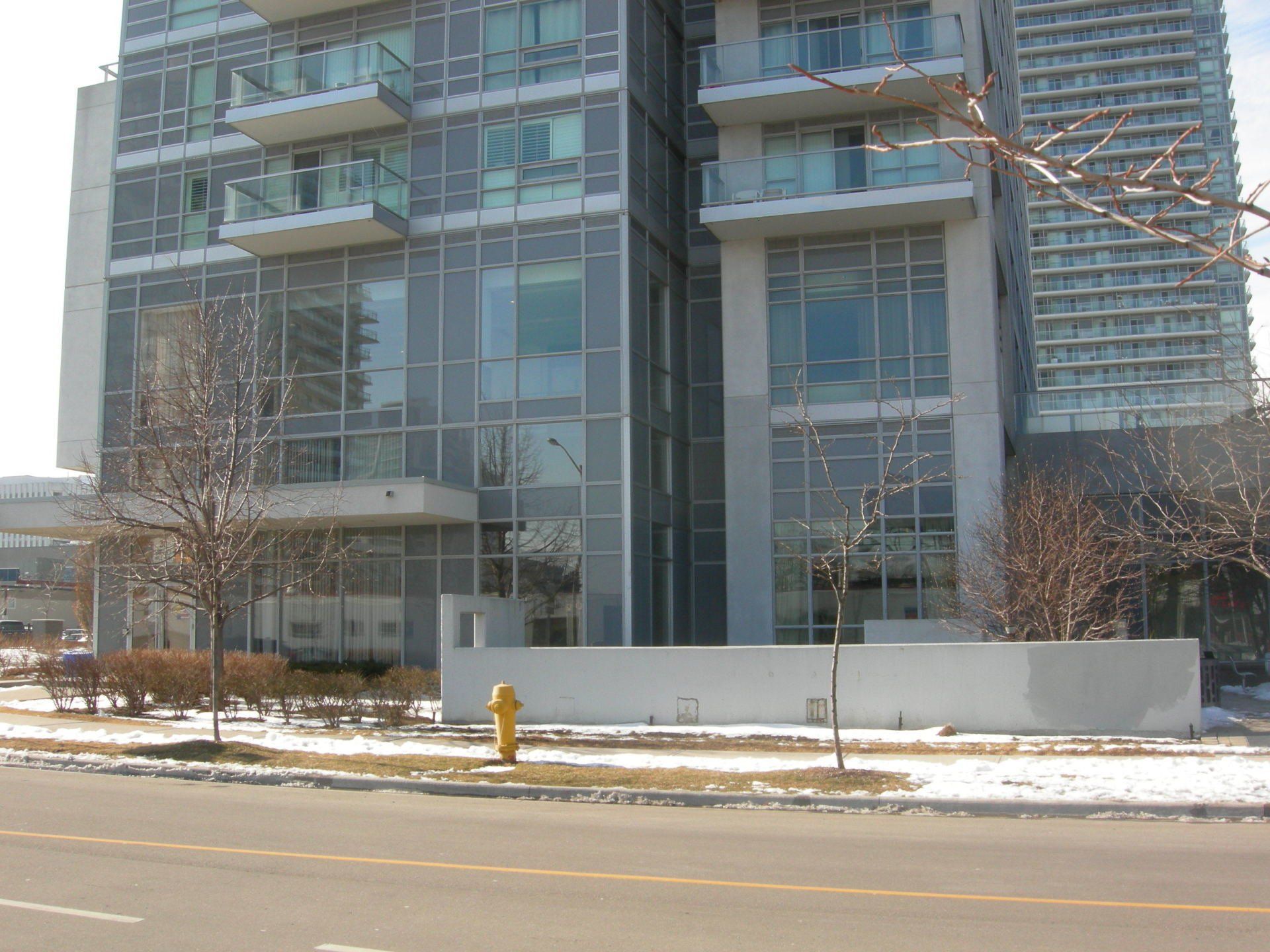A modern gray mid-rise apartment building with balconies and large windows stands behind a street with a fire hydrant.
