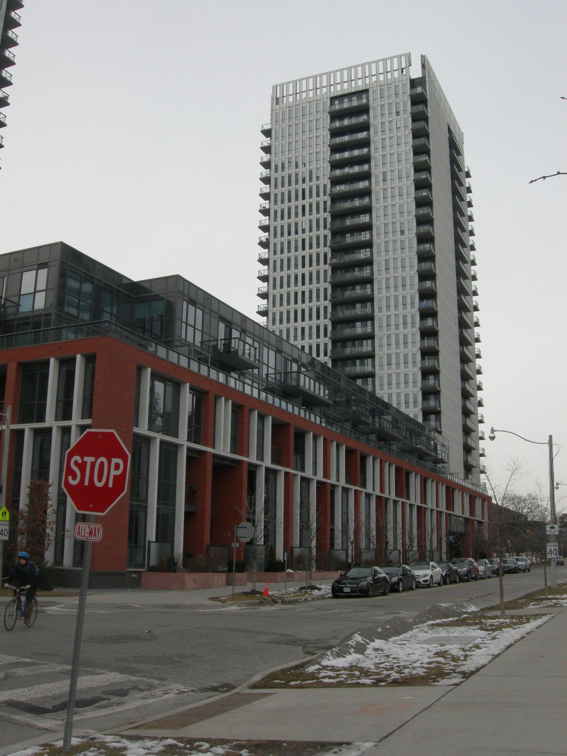 A tall white skyscraper rises behind a long, modern brick apartment building with a stop sign in the foreground.