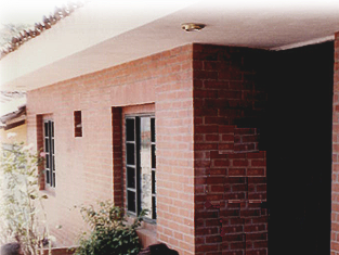 A red brick house exterior with two windows and a recessed dark entrance under a light-colored overhang.
