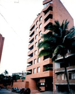 A tall, reddish-brown brick apartment building with recessed balconies and a palm tree in the foreground.