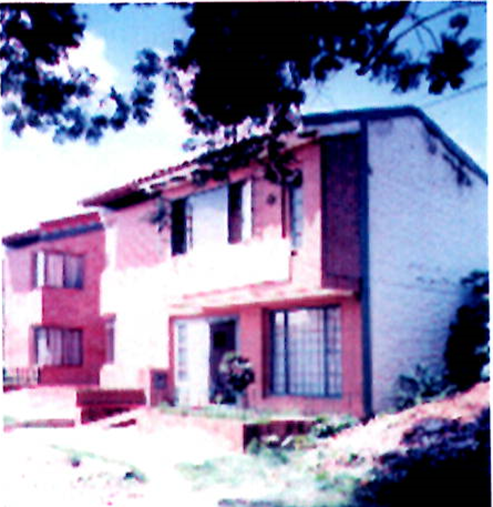 A two-story red-brick house with light-colored panels under a sloped roof, viewed from an outdoor setting.